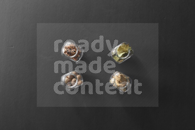 أوراق الغار وزنجبيل مجفف وقرفة وجوزة الطيب في أوعية زجاجية علي خلفية سوداء