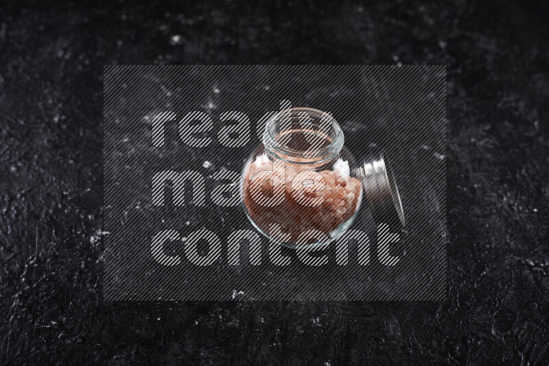 A glass jar full of coarse himalayan salt crystals on black background
