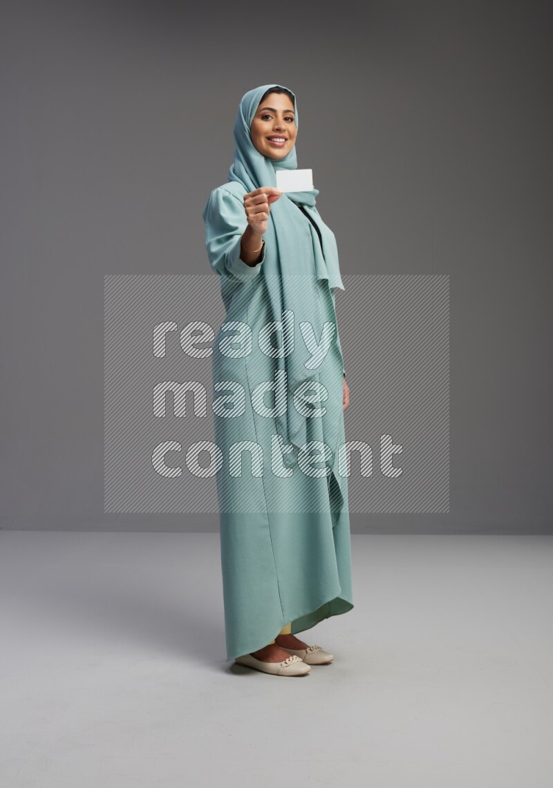Saudi Woman wearing Abaya standing holding ATM card on Gray background