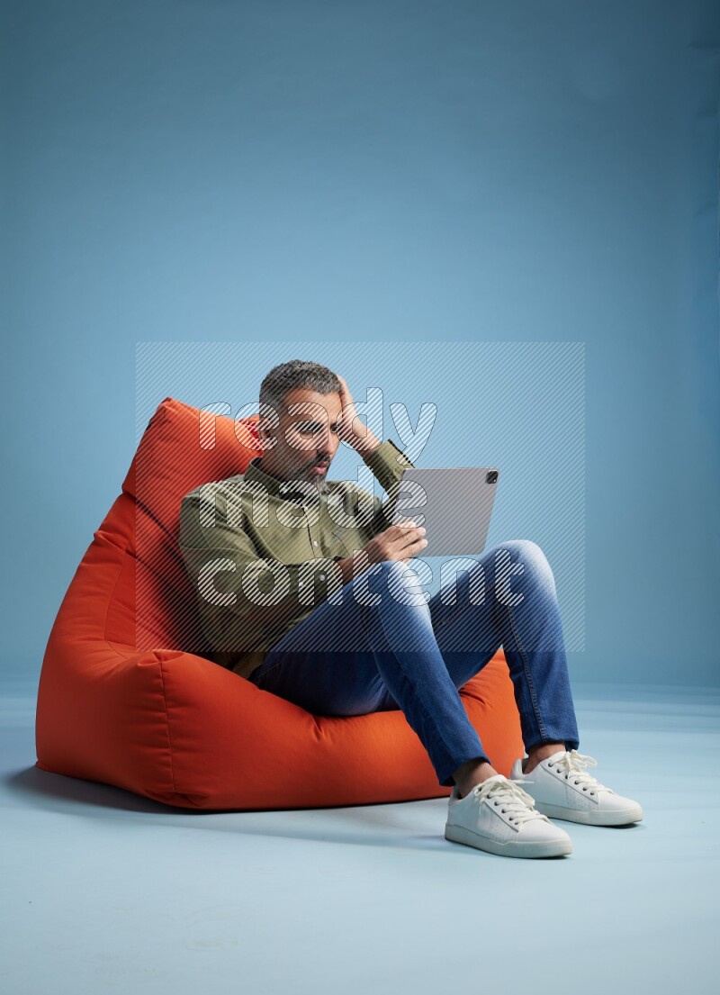 A man sitting on an orange beanbag and working on tablet