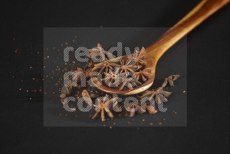 يانسون نجمي في مغرفة خشبية مع المزيد من اليانسون على خلفية سوداء