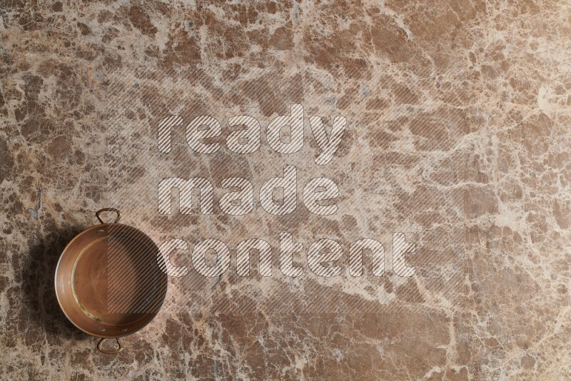A small copper pan on beige marble background
