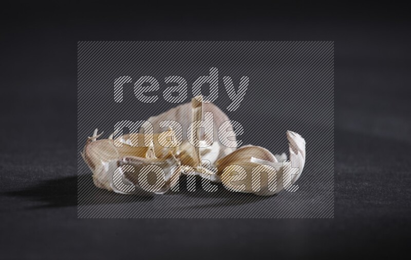 A cracked garlic bulb showing the cloves inside it on a black flooring