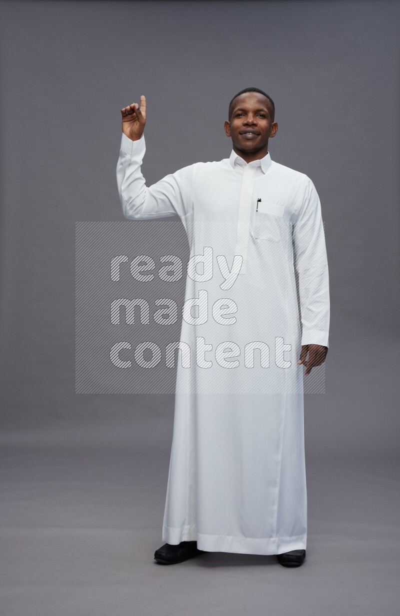 Saudi man wearing thob standing interacting with the camera on gray background