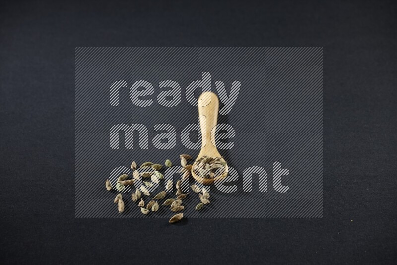 A wooden spoon full of cardamom on black flooring