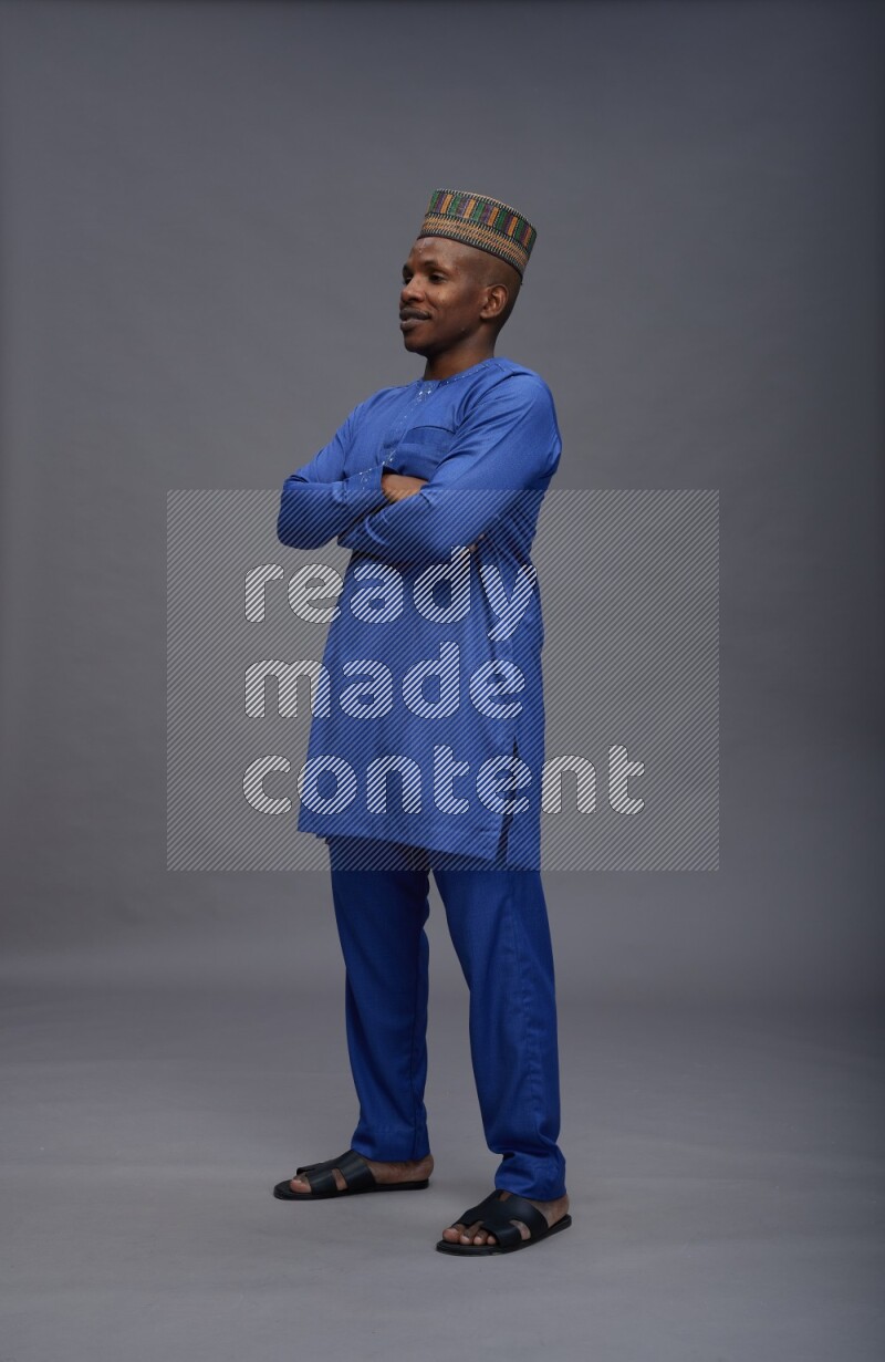 Man wearing Nigerian outfit standing with crossed arms on gray background