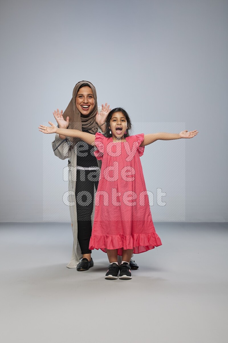 A girl and her mother interacting with the camera on gray background