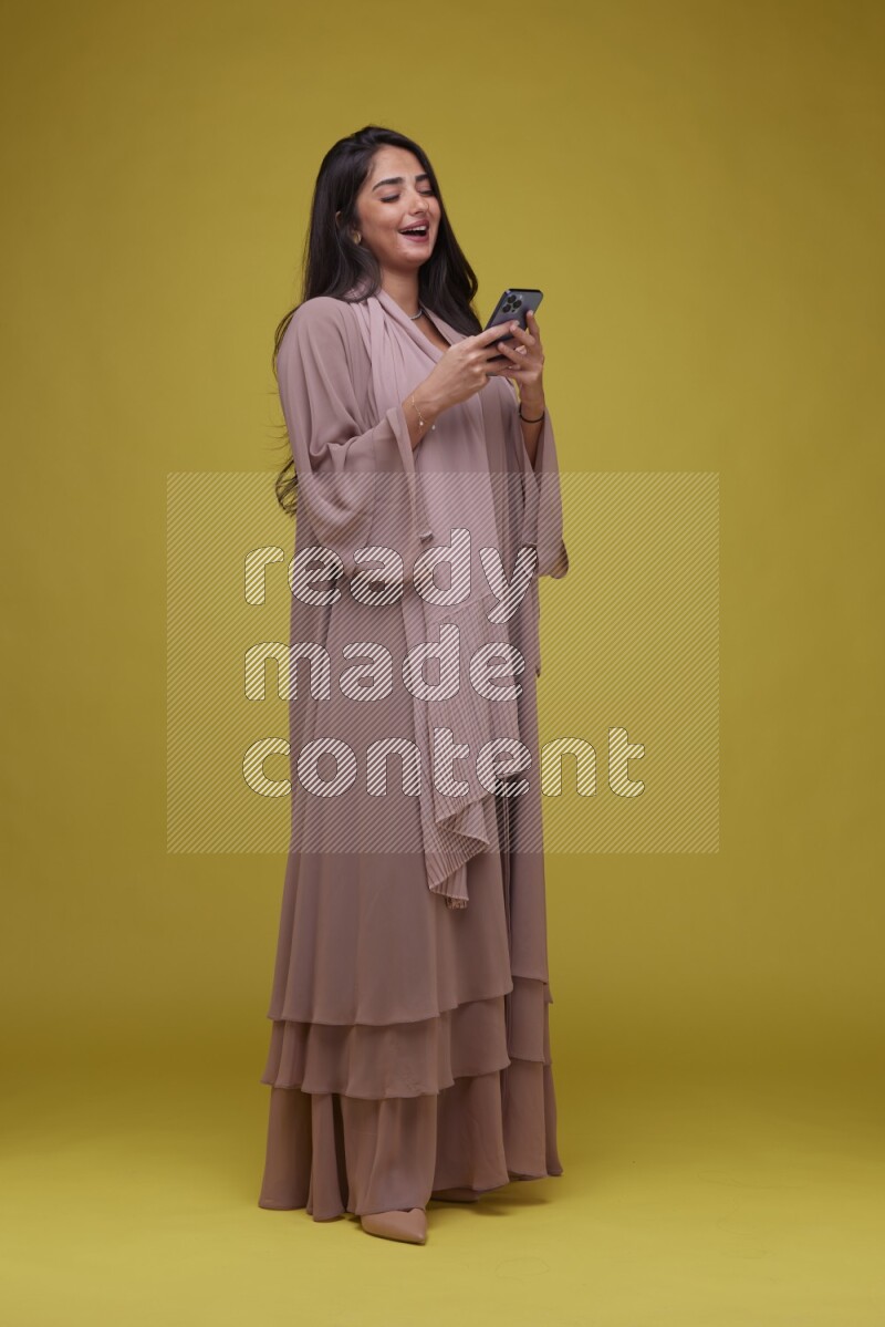 A woman Texting on a Yellow Background wearing Brown Abaya