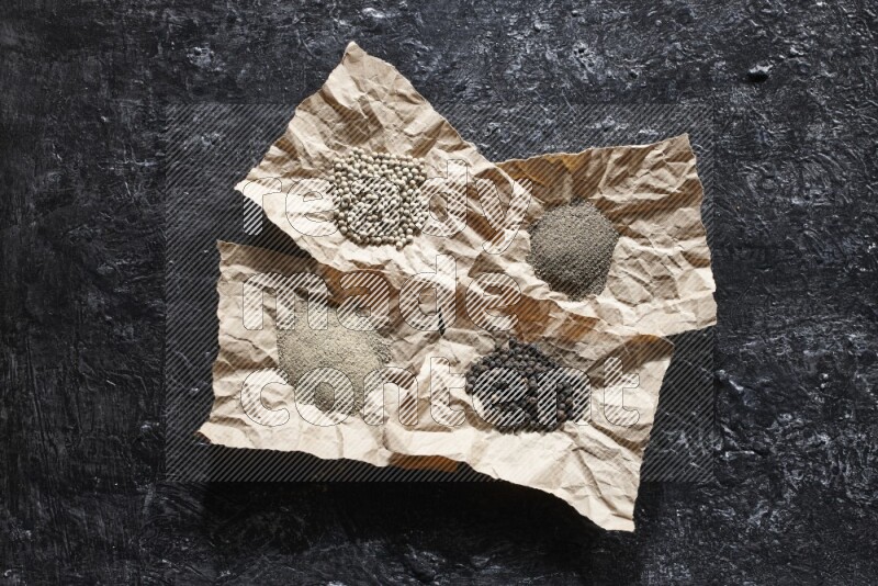 Crumpled pieces of paper full of black and white pepper beads and powder on a textured black flooring