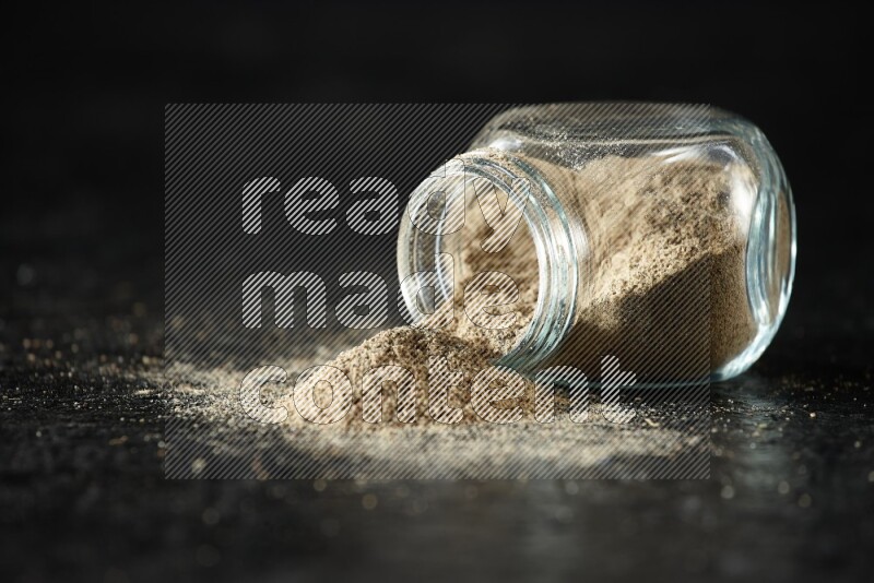 وعاء زجاجي للتوابل مقلوب ممتلئ ببودرة الهيل على خلفية سوداء