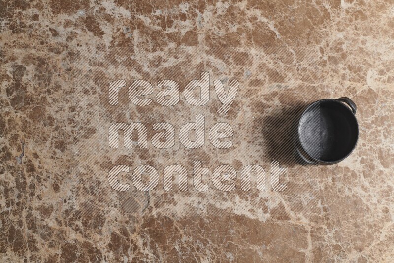 A black pottery bowl on beige marble background