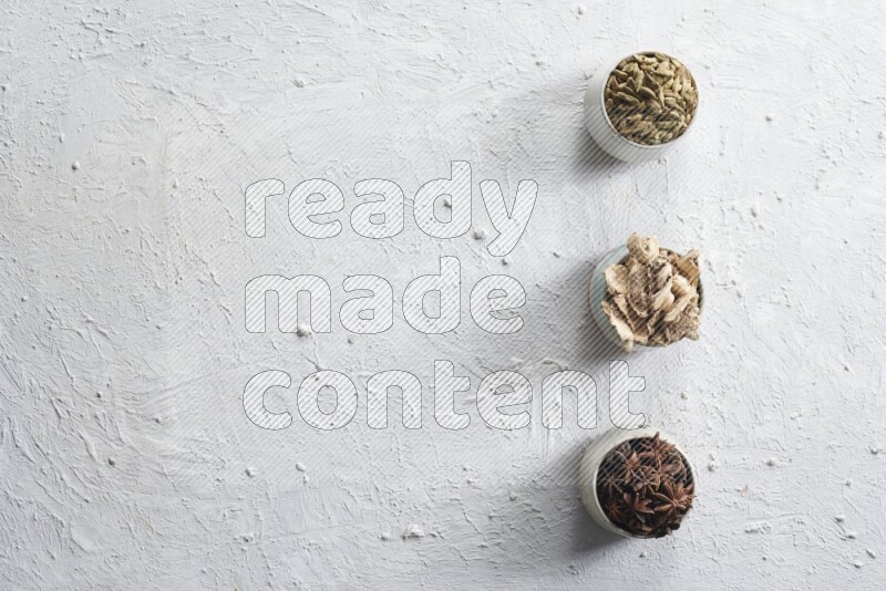 Cardamom, ginger and star anise in 3 bowls on a textured white background