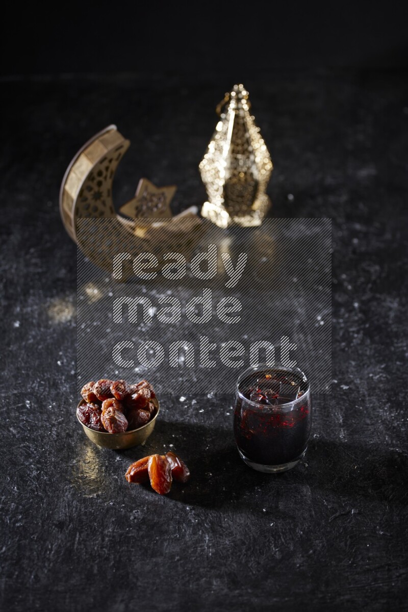 Dates in a metal bowl and tamarand beside a gold crescent and a lantern in a dark setup