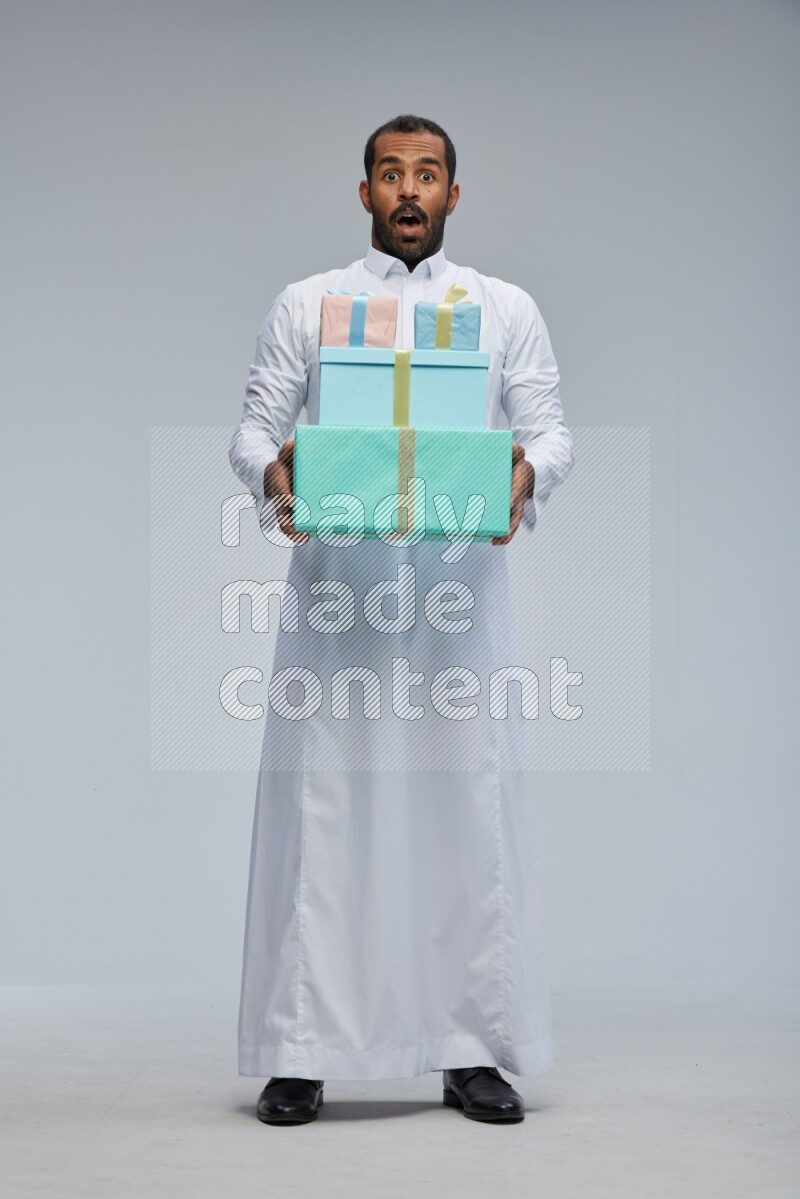 Saudi man Wearing thob standing holding gift box on Gray background