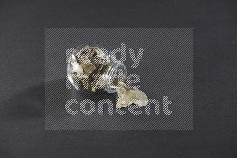 وعاء زجاجي ممتلئ بأوراق الغار والوعاء مقلوب وبعض الأوراق متناثرة خارجه علي خلفية سوداء