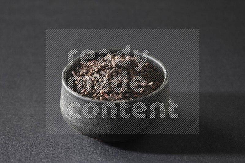 A black pottery bowl full of cloves on a black flooring