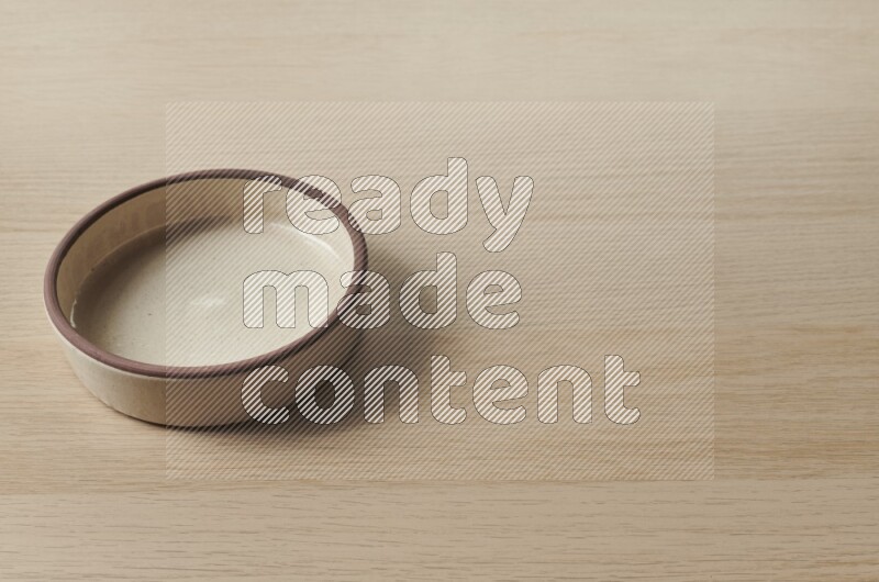 A beige pottery oven bowl on light wooden background