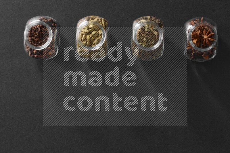 قرنفل وحبوب الهيل وريحان مجفف ويانسون نجمي في أوعية زجاجية علي خلفية سوداء