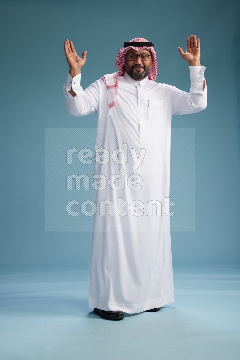 Saudi Man with shimag Standing Interacting with the camera on blue background