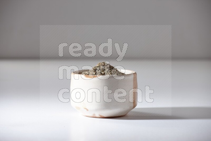 A beige bowl full of cumin seeds on a white flooring