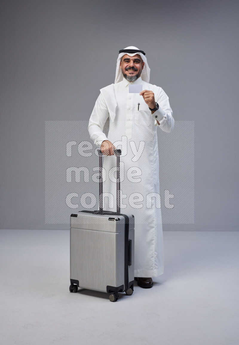 رجل سعودي يرتدي ثوب ابيض ويحمل بطاقة بنكية وبجواره حقيبة سفر