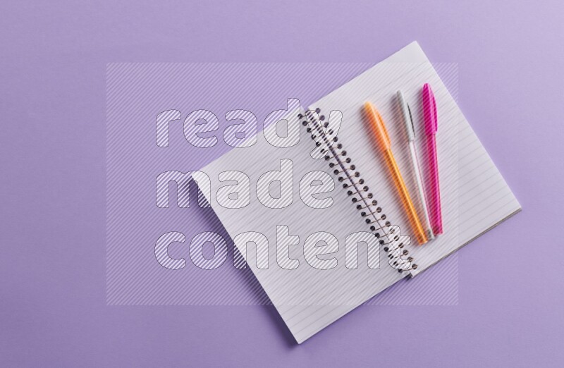 A blank open notebook with school supplies on purple background
