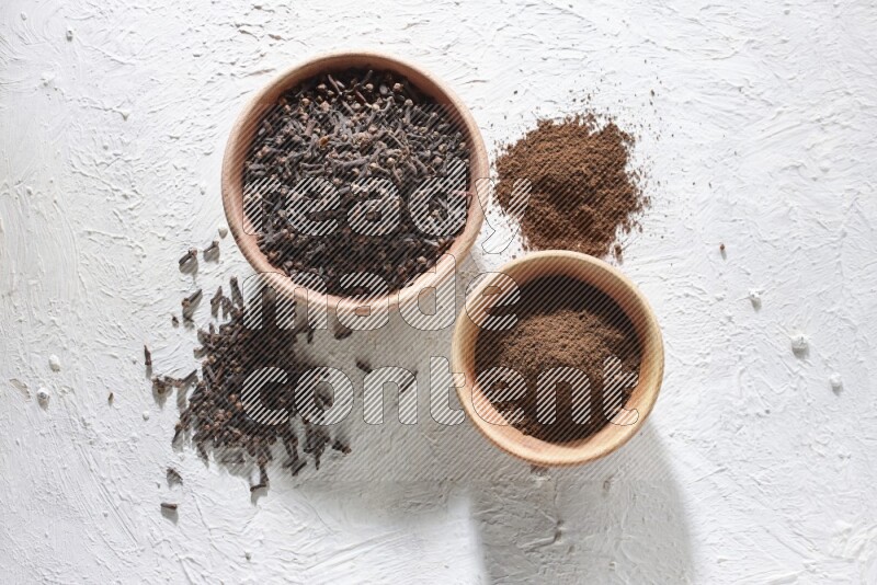 2 wooden bowls full of cloves powder and whole cloves on a textured white flooring