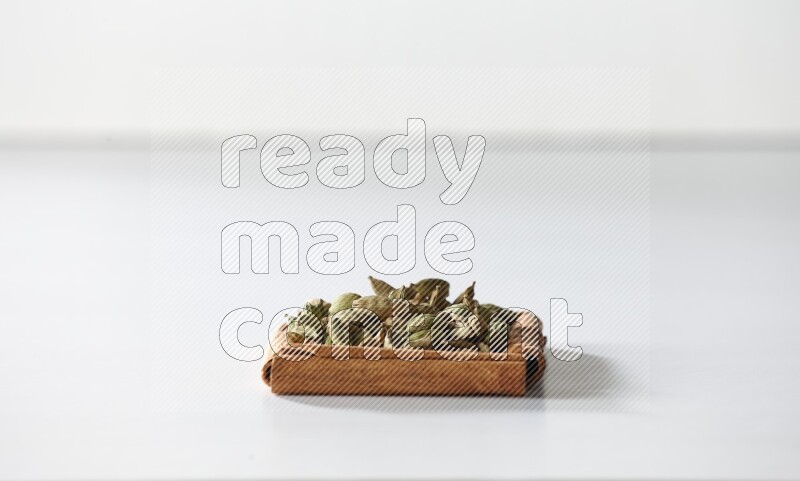 أربعة من أعواد القرفة مكونة شكل مربع بداخلها حبوب الهيل علي خلفية بيضاء