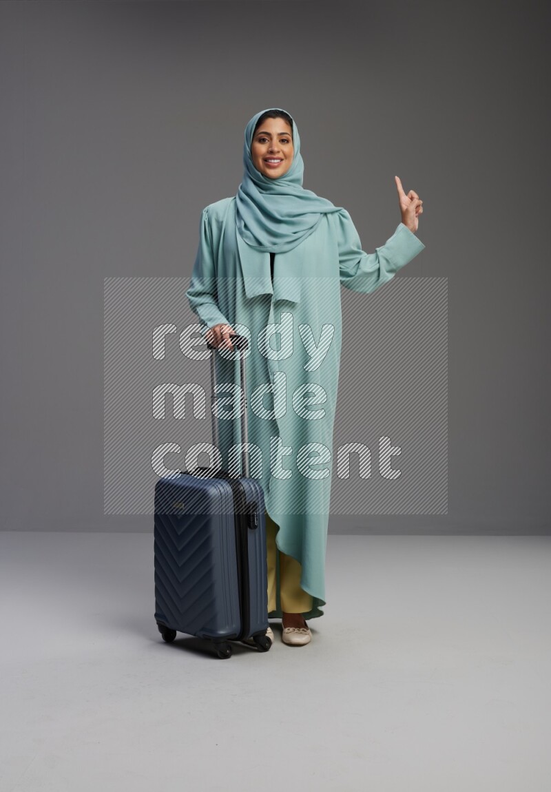 Saudi Woman wearing Abaya standing holding Travel bag on Gray background
