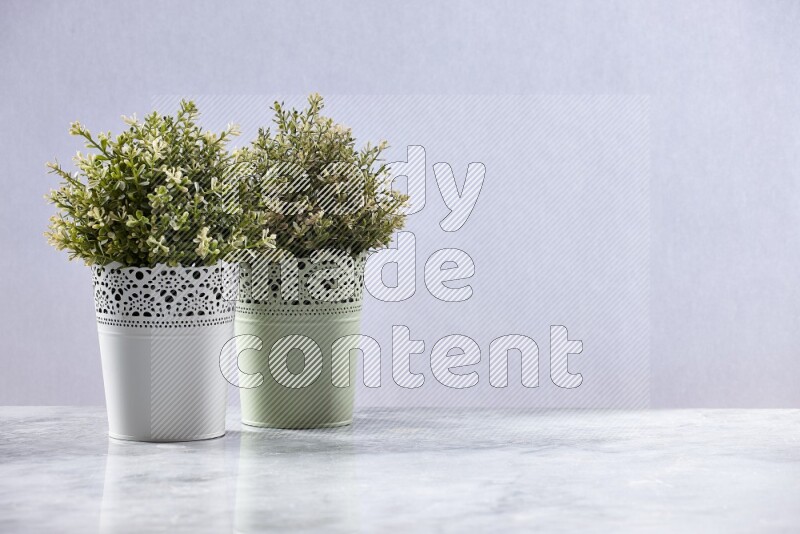 Two different artificial plants in white and green decorative pots on grey marble background