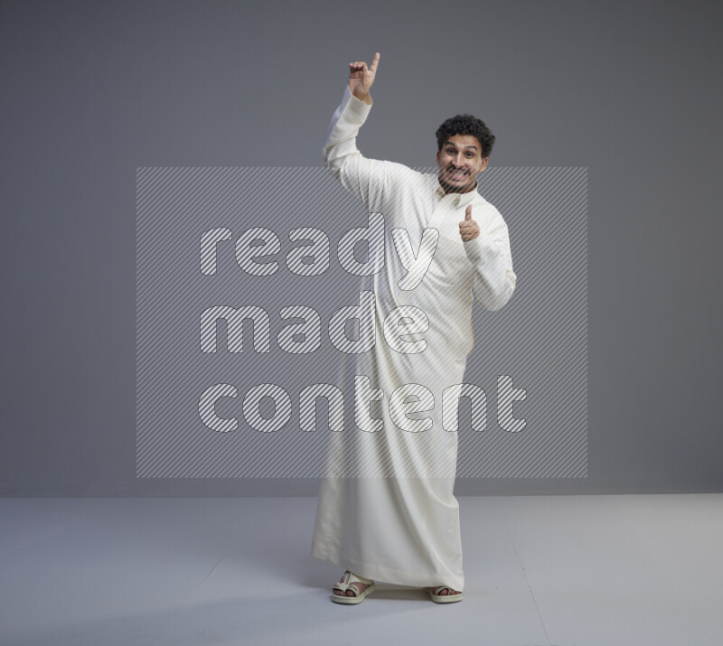 A Saudi man standing wearing thob interacting with the camera on gray background