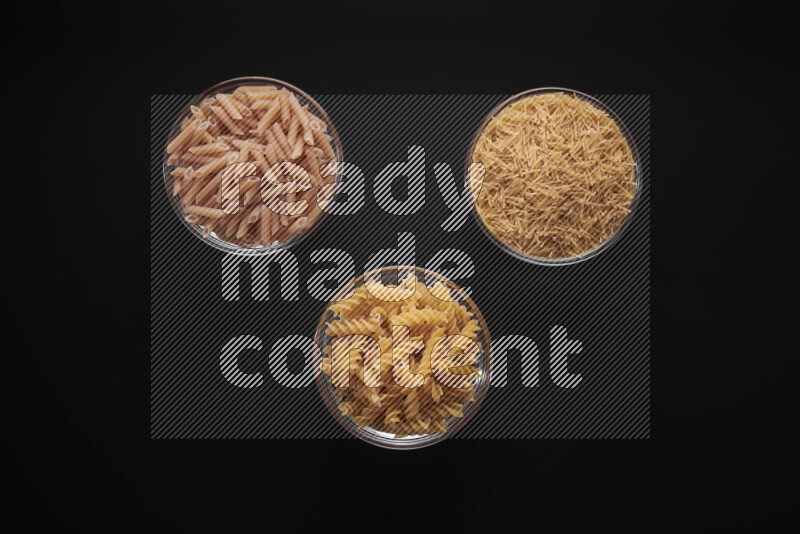 Different pasta types in glass bowls on black background