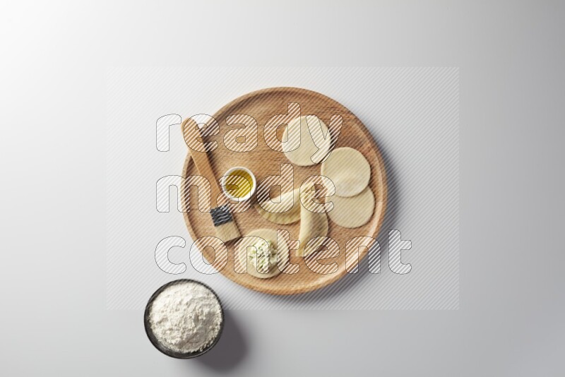 two closed sambosas and one open sambosa filled with cheese while flour, and oil with oil brush aside in a wooden dish on a white background