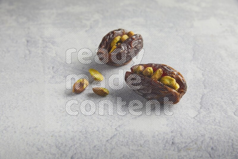 two pistachio stuffed madjoul date on a light grey background