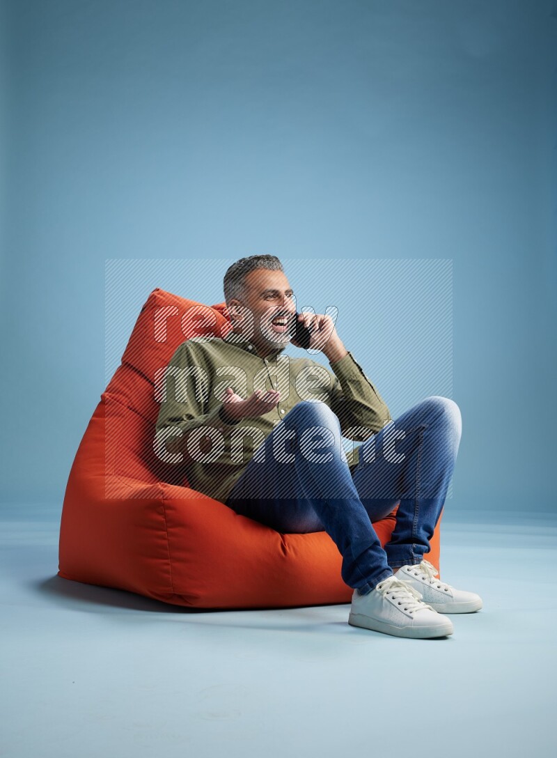 A man sitting on an orange beanbag and talking on the phone