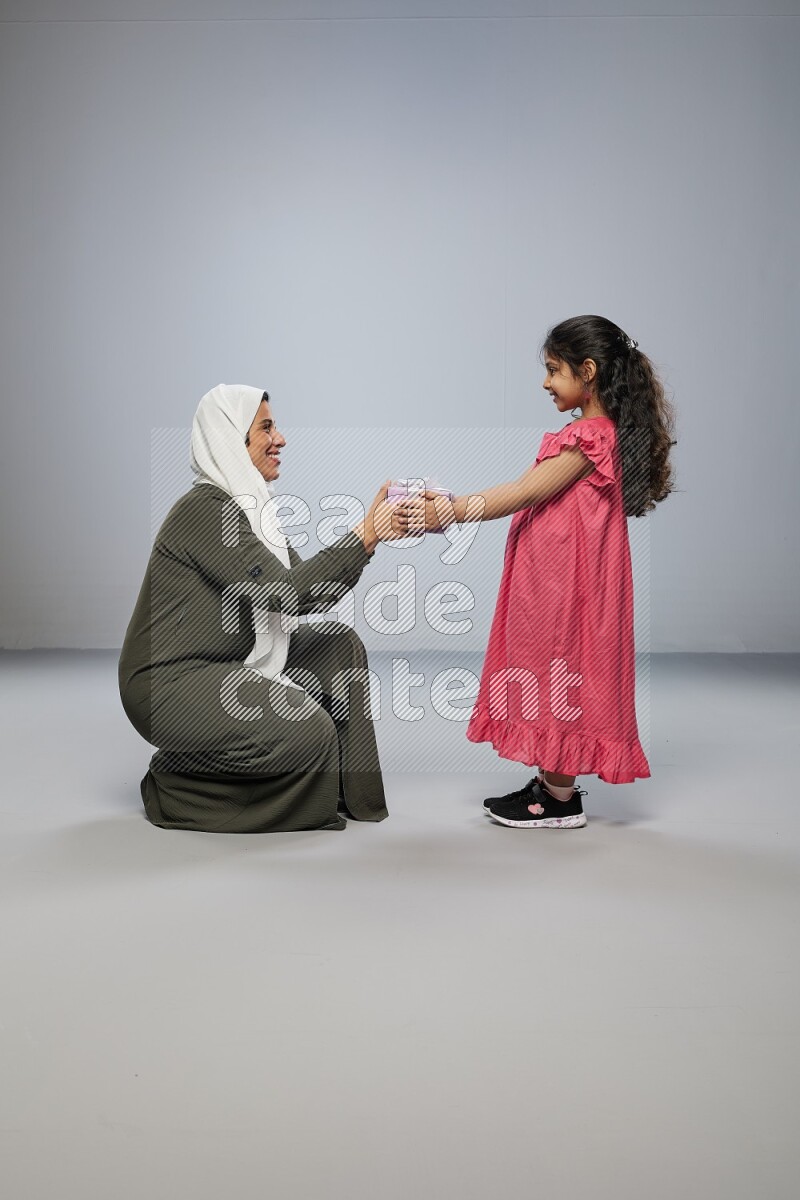 A girl giving a gift to her mother on gray background