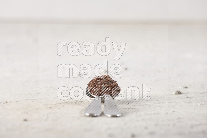 2 metal spoons full of flax seeds on a textured white flooring