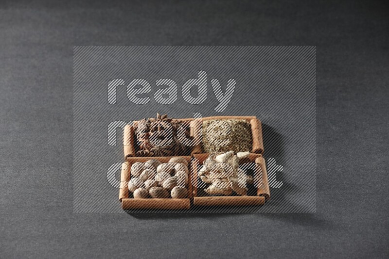 4 مربعات من عيدان القرفة ممتلئة باليانسون النجمي والكمون والزنجبيل المجفف وجوزة الطيب على أرضية سوداء