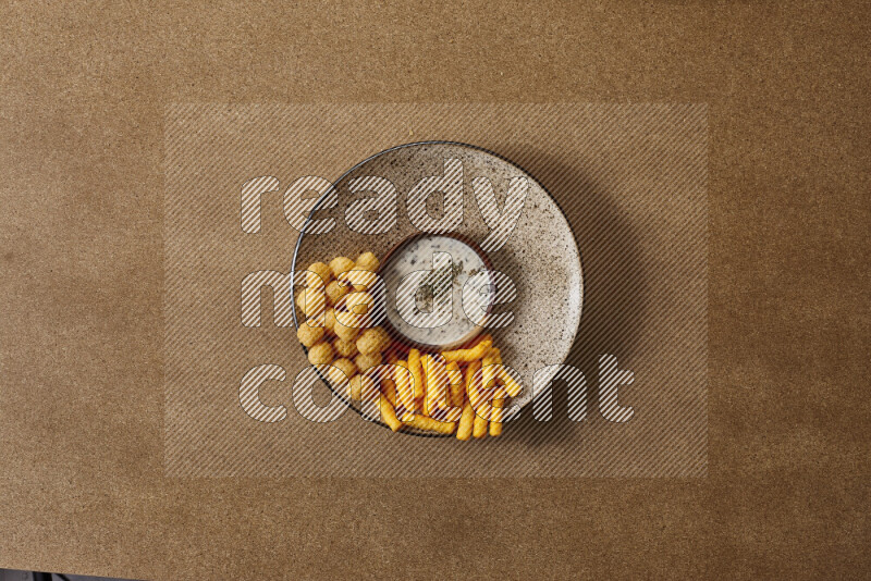 Assorted snacks on a pottery plate with a dipping on brown background