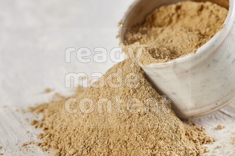 A beige pottery bowl full of ground ginger powder with fallen powder from it on white background