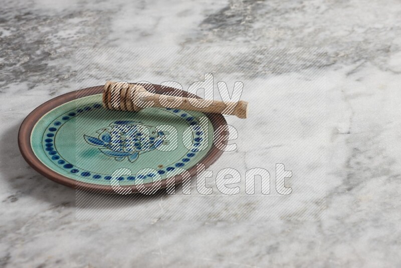 Decorative pottery plate with wooden honey dipper in it on grey marble background