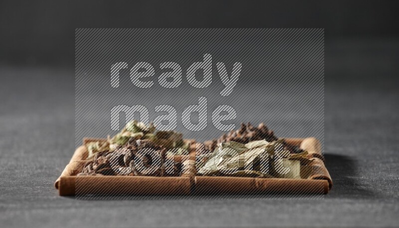 4 squares of cinnamon sticks full of star anise, cardamom, cloves and bay laurel leaves on black flooring