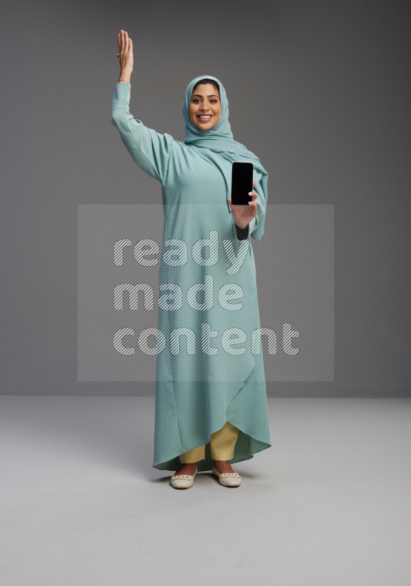 Saudi Woman wearing Abaya standing showing phone to camera on Gray background