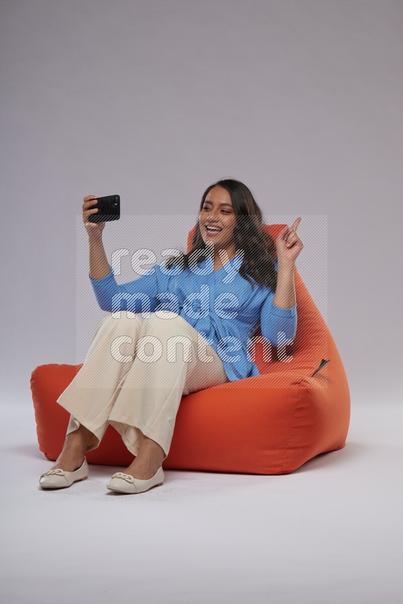 A woman sitting on an orange beanbag and taking selfie