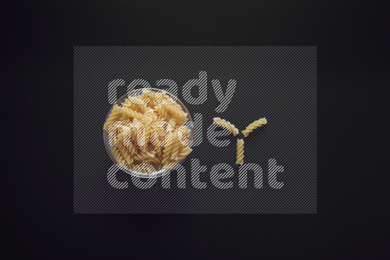 Fusilli pasta in a glass bowl on black background
