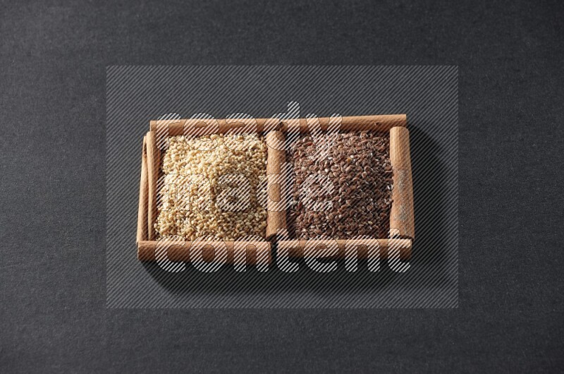 مربعان من أعواد القرفة ممتلئان ببذور الكتان وبذور السمسم علي خلفية سوداء