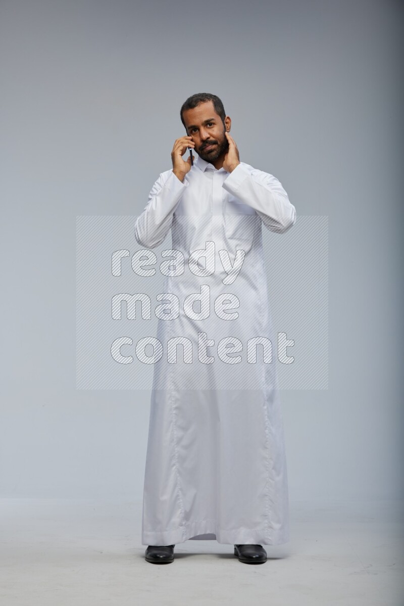Saudi man wearing Thob standing talking on phone on Gray background