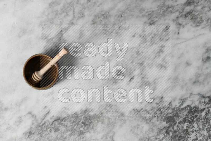 Multicolored pottery bowl with wooden honey dipper in it on grey marble background