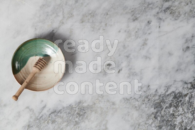 طبق فخاري متعدد الألوان مع ملعقة عسل خشبية بداخله على خلفية من الرخام الرمادي