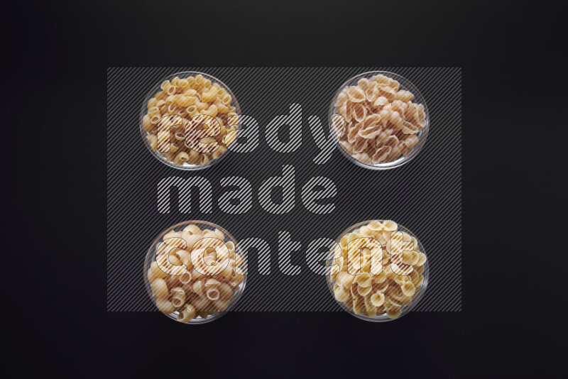 Different pasta types in glass bowls on black background